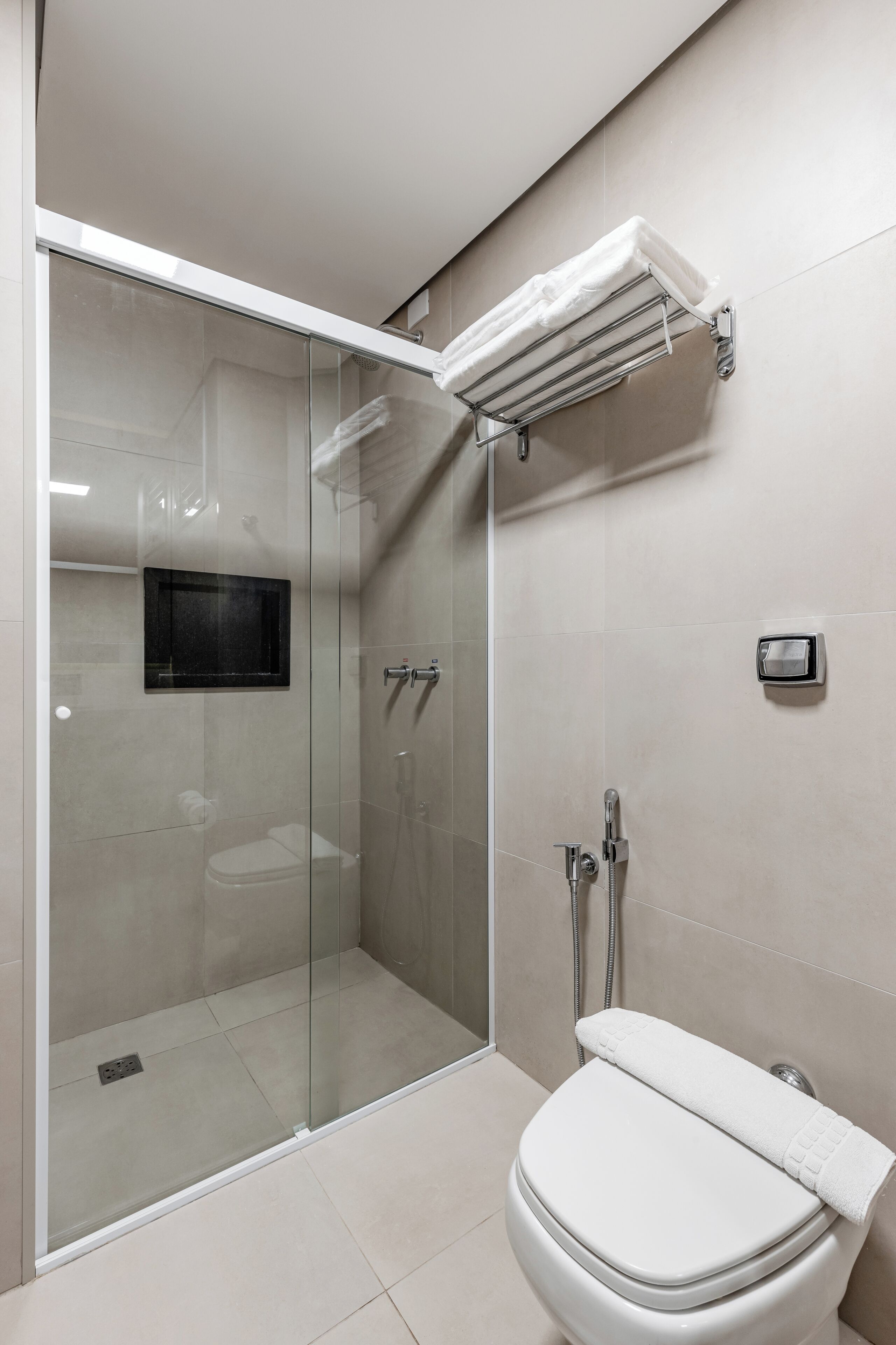Un baño moderno con ducha de vidrio, inodoro con una toalla encima y toallero adherido a la pared.
