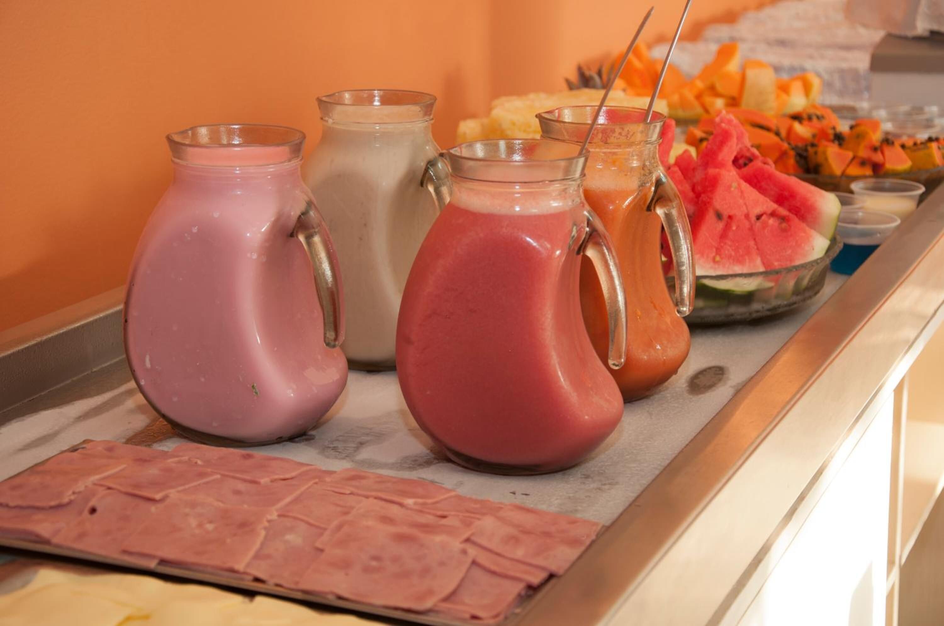 Buffet com diversas bebidas em jarras e uma seleção de frutas e vegetais.