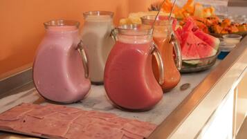 Buffet com diversas bebidas em jarras e uma seleção de frutas e vegetais.