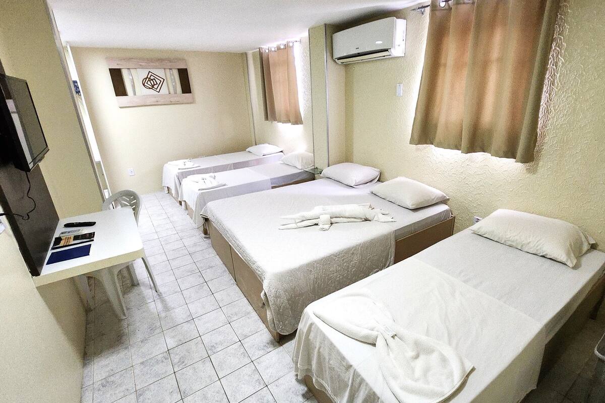 Ein Hotelzimmer mit drei Einzelbetten, einem Schreibtisch mit Stuhl, einem Fernseher und einer Klimaanlage.