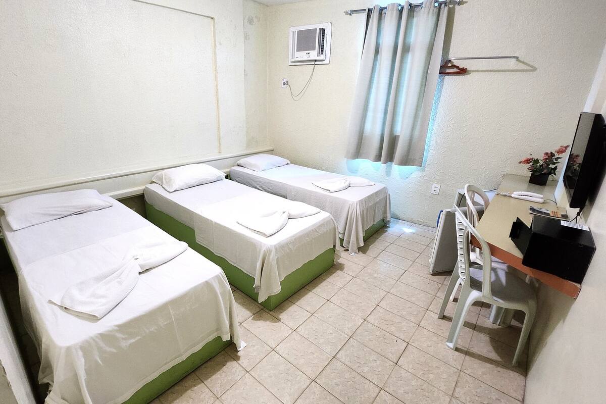 Ein Zimmer mit zwei Einzelbetten, einem Schreibtisch mit Stuhl, einem kleinen Tisch mit einer Vase und einem Fernseher.