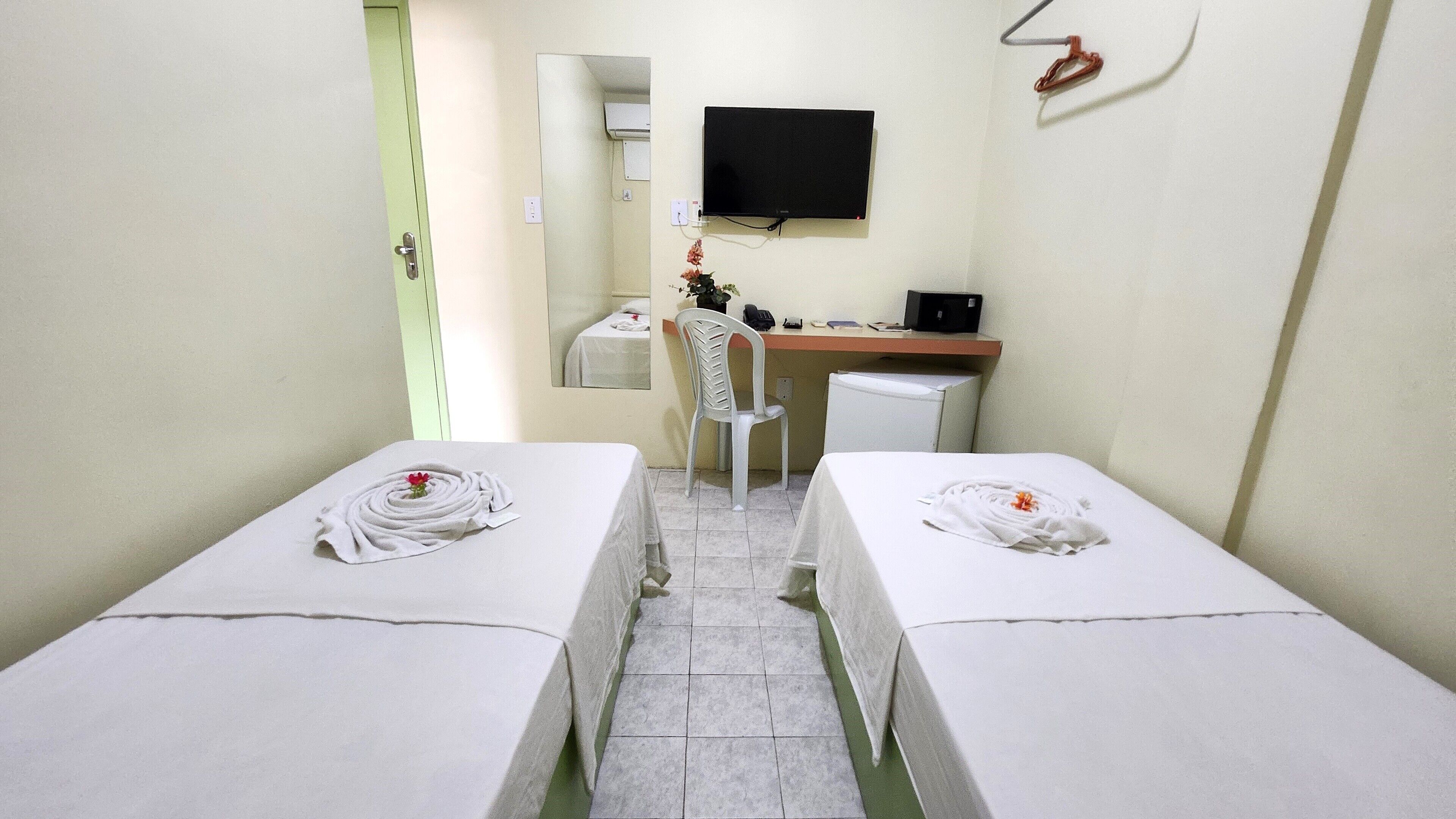 Ein Hotelzimmer mit zwei Betten, einem Schreibtisch, einem Sessel, einem Fernseher und einer kleinen Küchenzeile.