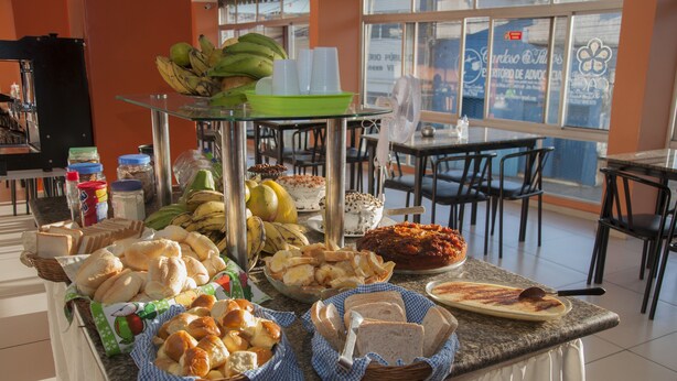 A buffet table with various food items including bread, fruits, and a dish with a red sauce. - Guarany Hotel Express (João Pessoa)