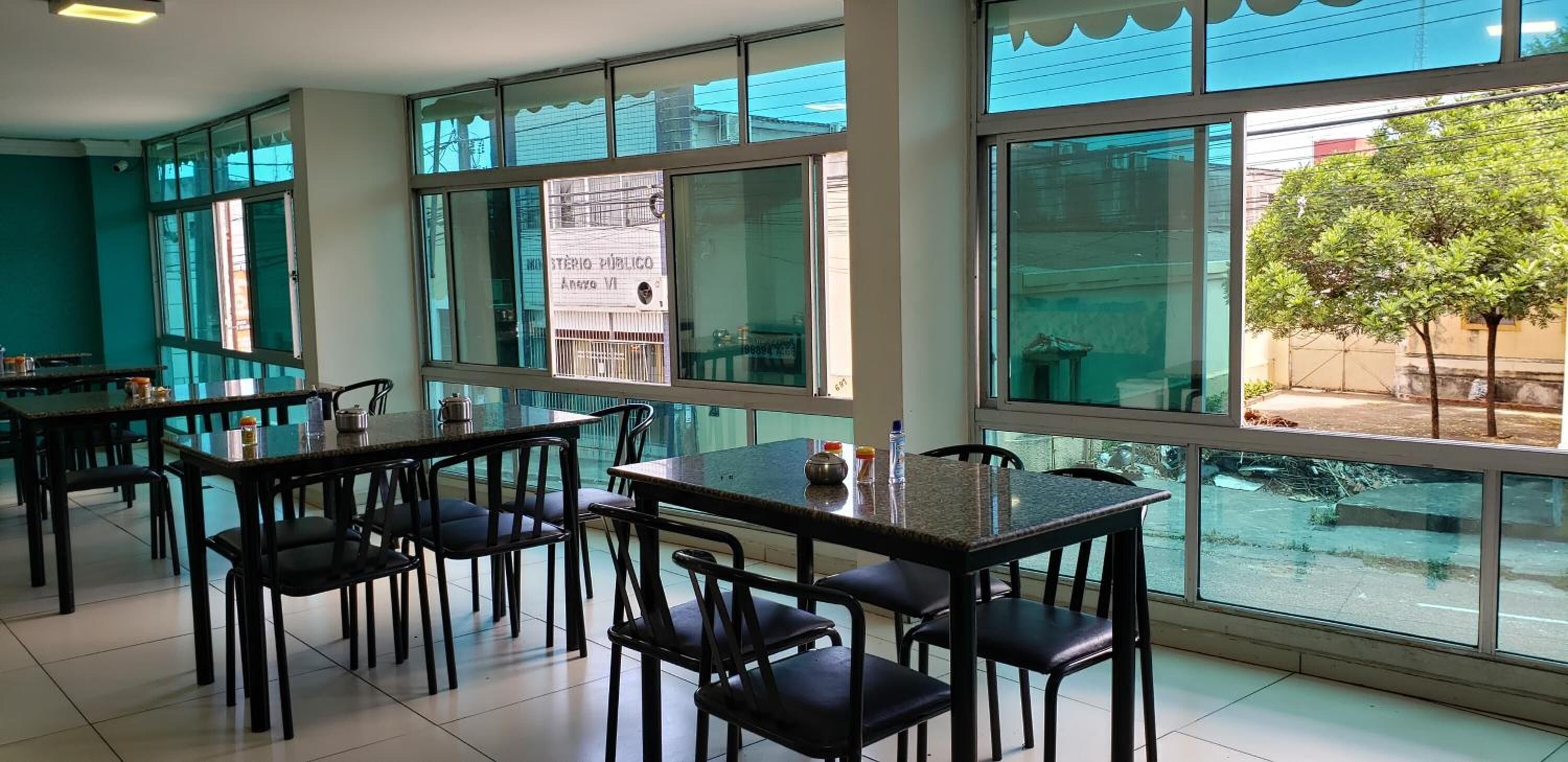 A dining area with tables and chairs, large windows with a view of the street, and a tiled floor.