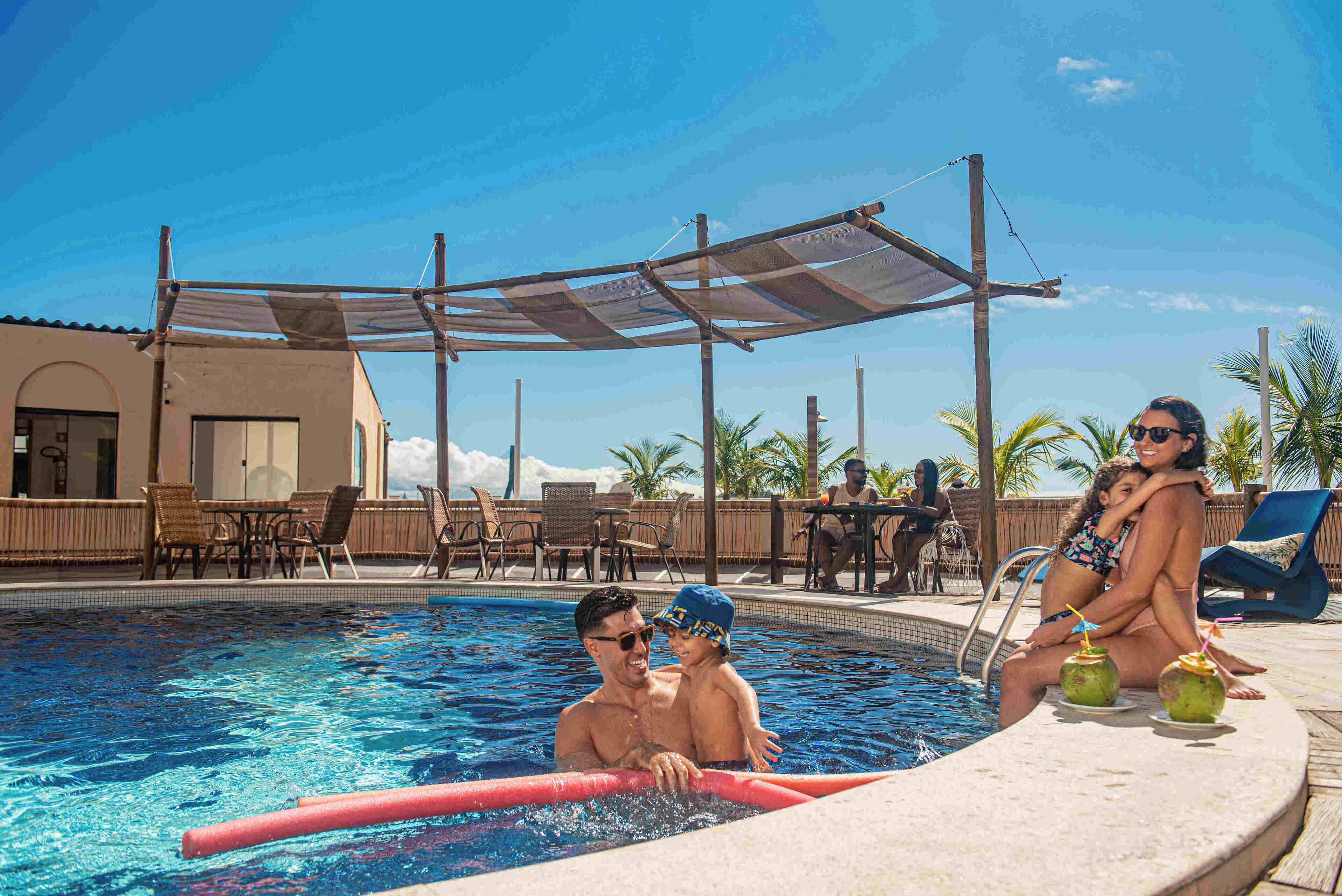 Un área de piscina con zona de estar a la sombra, sillones de descanso y un bar junto a la piscina.