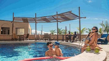 Un área de piscina con zona de estar a la sombra, sillones de descanso y un bar junto a la piscina.