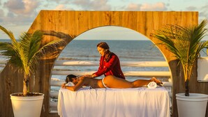 A massage therapy session on a beach with a wooden archway, palm trees, and a view of the ocean. - Opaba Praia Hotel (Ilhéus)
