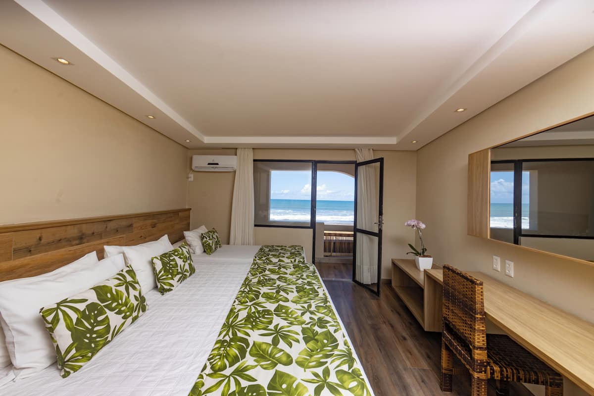 A bedroom with a large bed, a wooden headboard, a desk, and a view of the ocean.