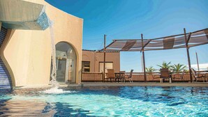 A pool area with a water feature, outdoor seating, and a covered patio. - Opaba Praia Hotel (Ilhéus)