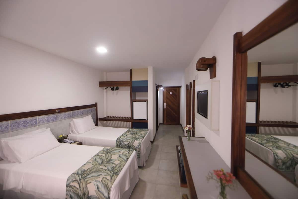 A hotel room with two beds, a wooden headboard, a mirror, and a small table with a vase.