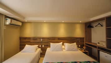 A hotel room with two single beds, a wooden headboard, a small desk with a phone and a vase of flowers, and a white air conditioning unit.