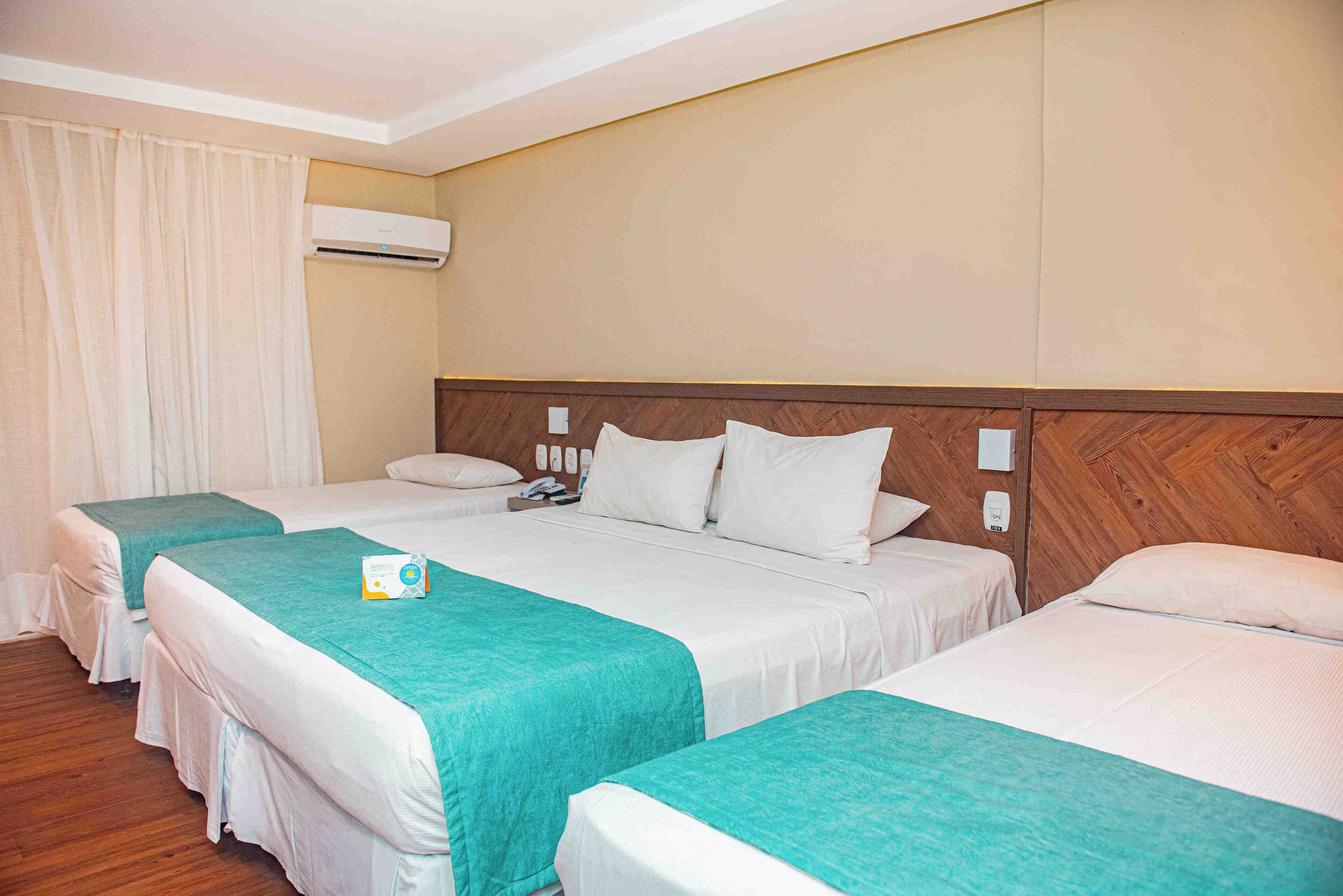 A hotel room with two beds, a wooden headboard, a white air conditioner, and a curtain.