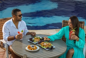 Guests can enjoy casual dining by the pool with a meal served at a round outdoor table.