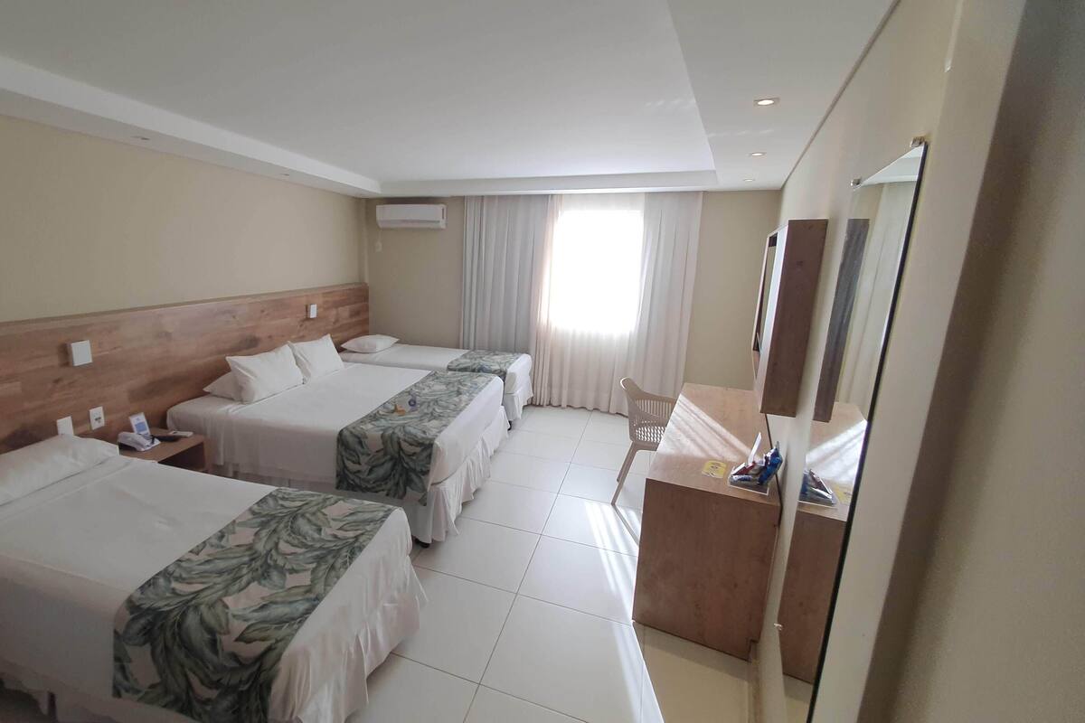 A hotel room with two beds, a wooden headboard, a desk with a mirror, and a window with curtains.