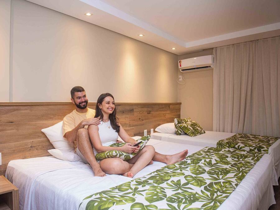 A hotel room with two beds, wooden headboard, white bedding, and a green leaf-patterned bedspread.