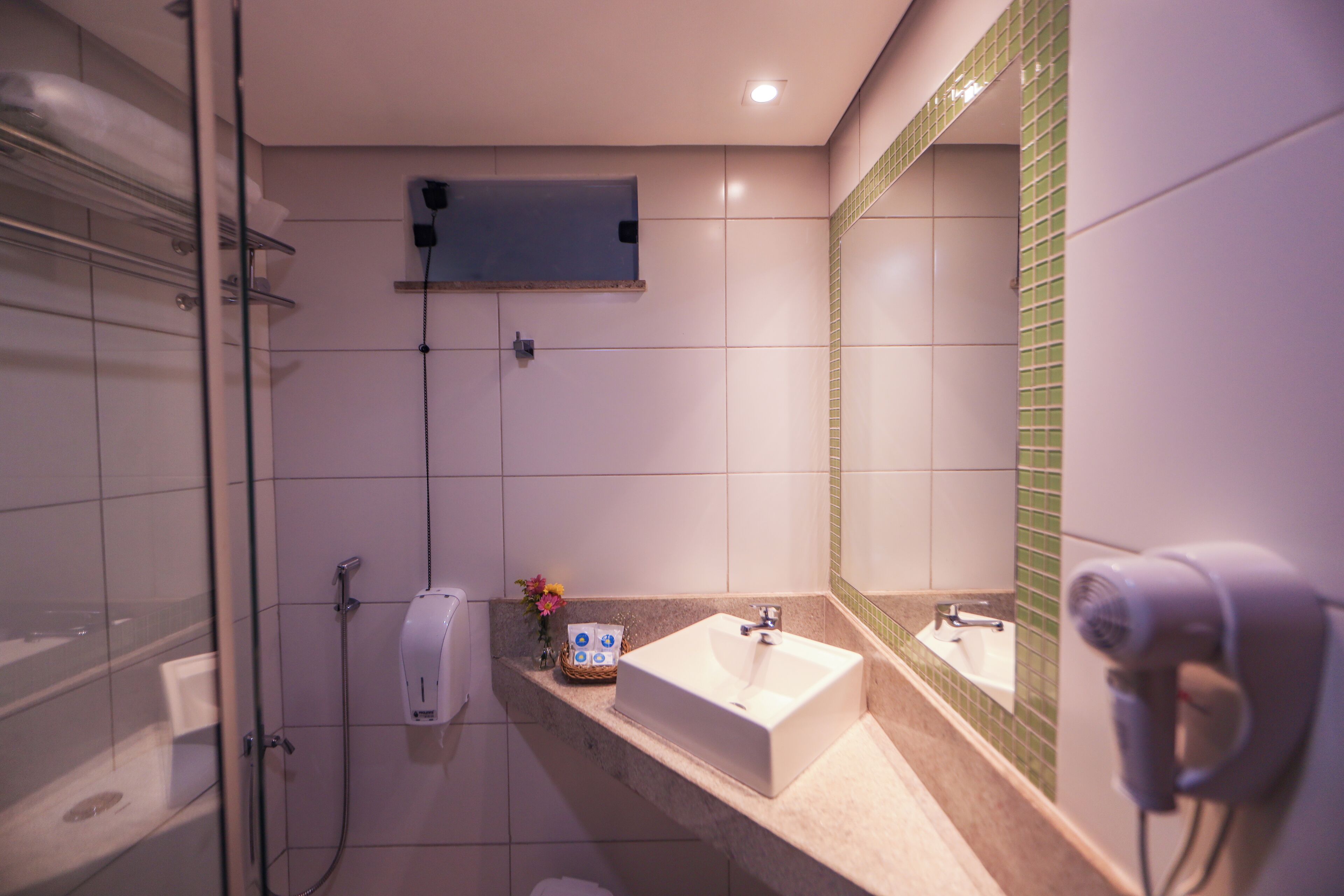 A bathroom with a glass shower enclosure, a sink with a mirror, and a hairdryer on the wall.