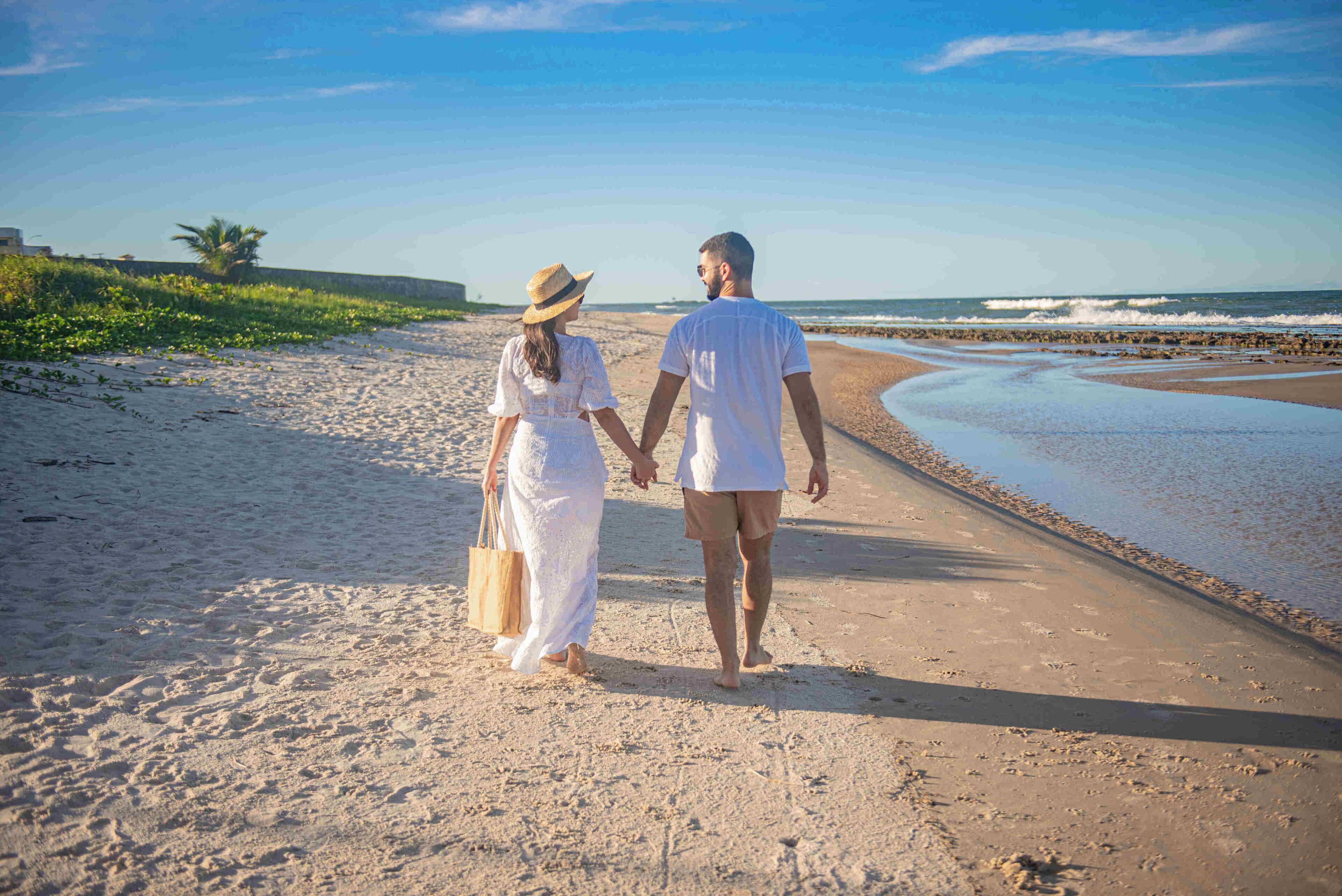 Um casal caminhando por um caminho de areia com vista para o oceano.