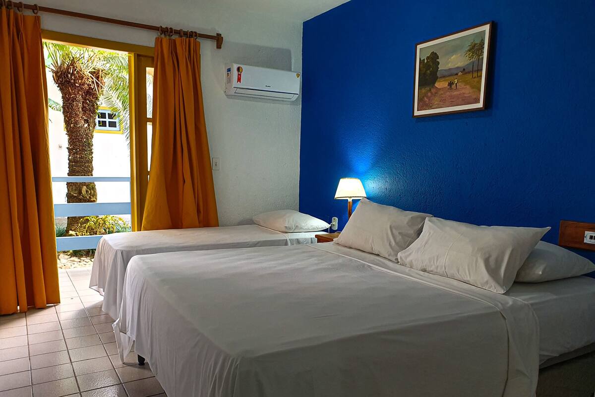 A hotel room with two beds, a nightstand, a lamp, an air conditioner, and a painting on the wall.