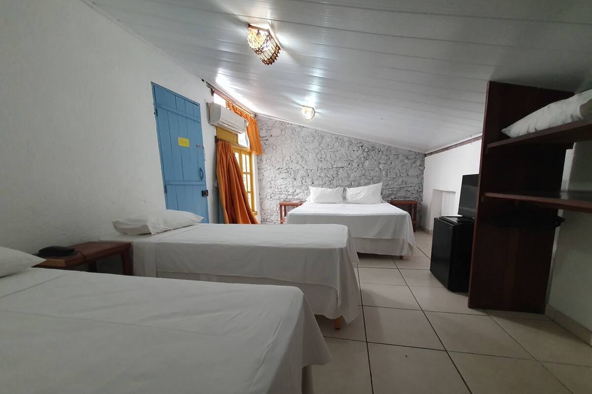 A hotel room with two beds, a blue door, an air conditioning unit, a stone wall, and a television.