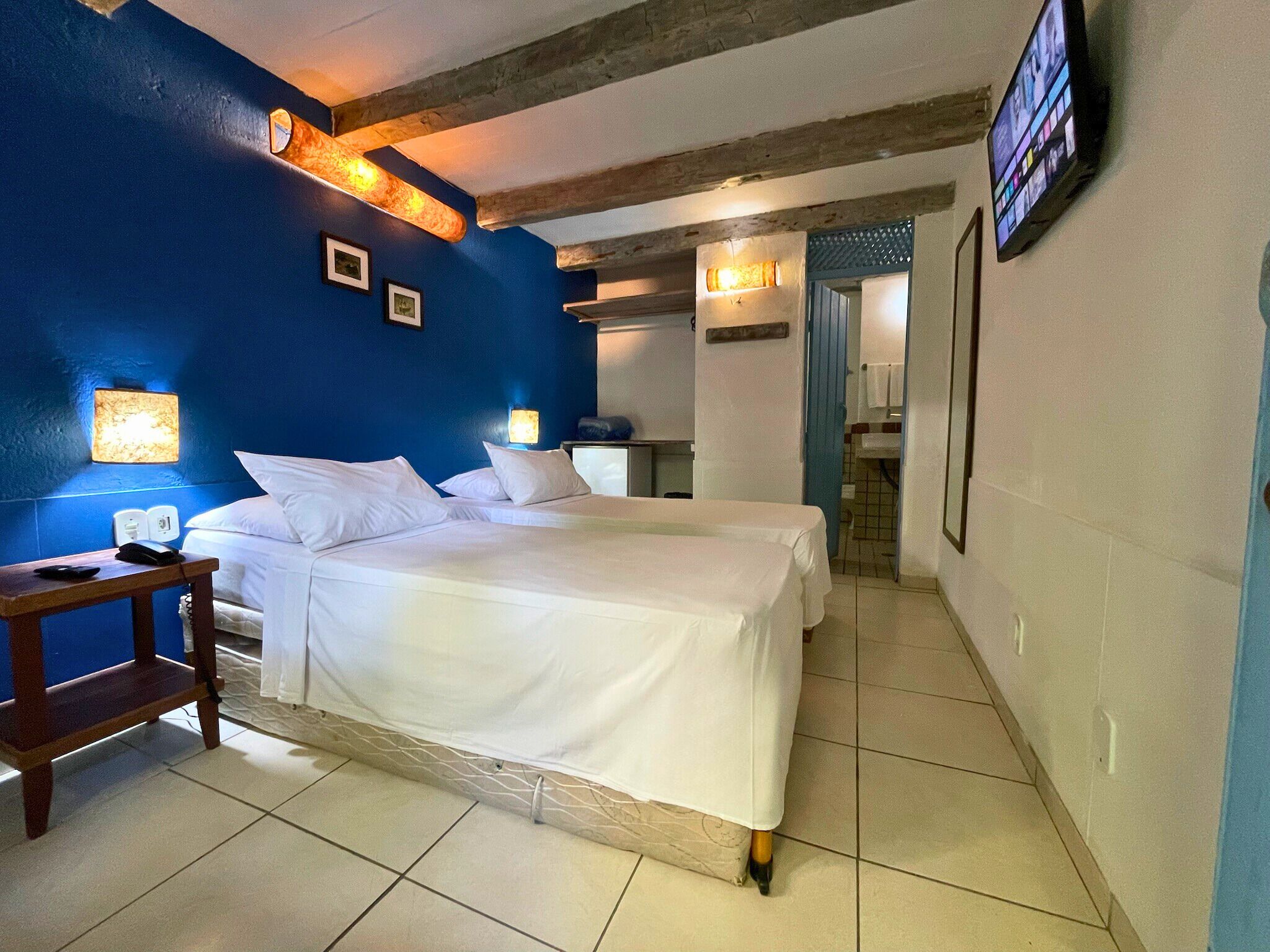 A hotel room with two beds, a wooden nightstand, a TV, and a bathroom visible through an open door.
