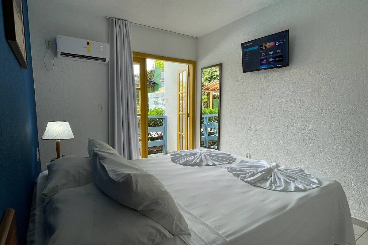 A hotel room with a bed, a TV, an air conditioner, and a view of the outdoors.