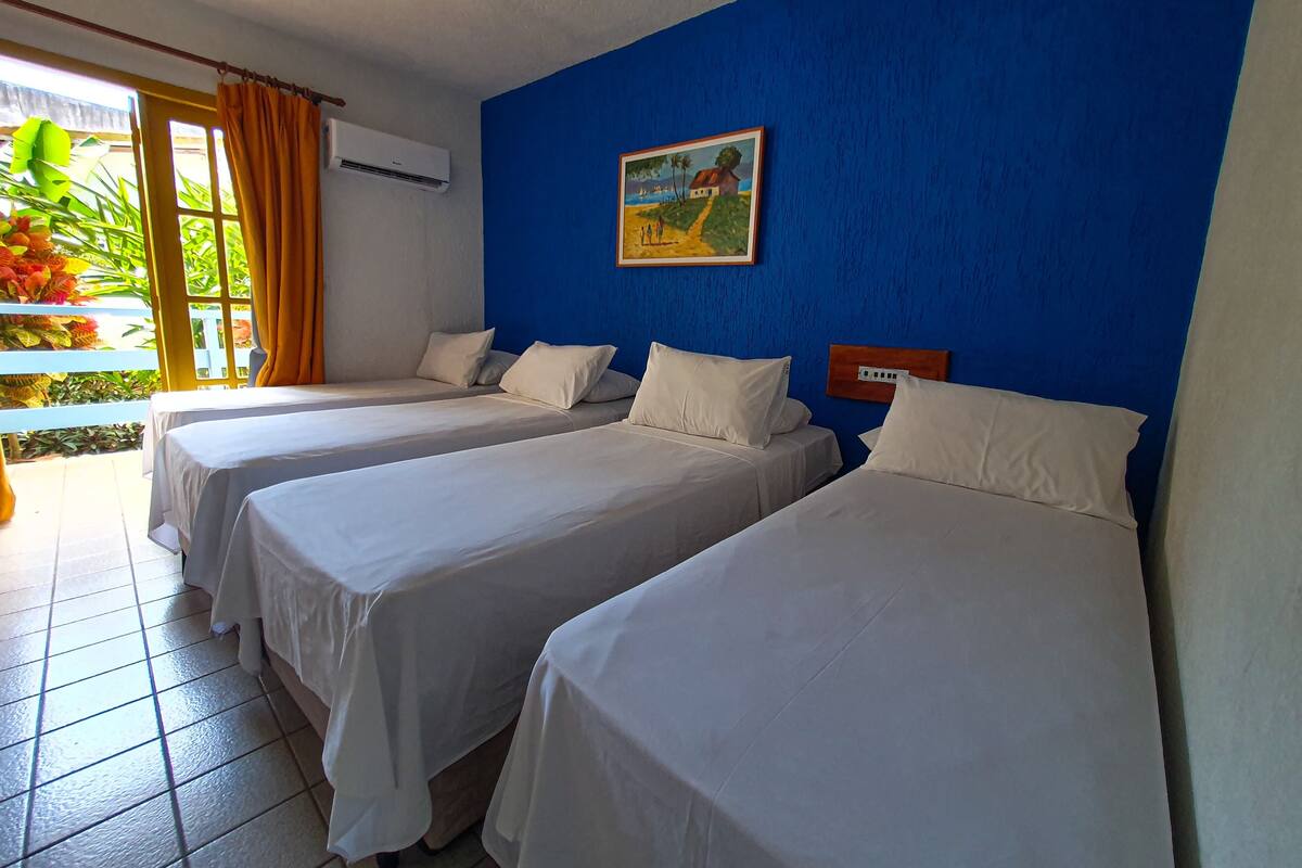 A hotel room with three beds, a blue wall, an air conditioning unit, and a painting.
