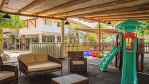 An outdoor patio area with wicker furniture, a play structure, and a building in the background.