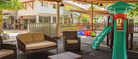 An outdoor patio area with wicker furniture, a play structure, and a building in the background.
