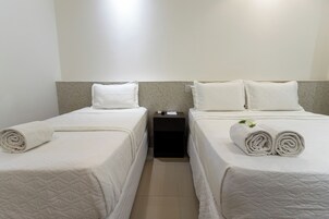 Ein Hotelzimmer mit zwei Betten, jeweils mit einem ordentlich gefalteten weißen Handtuch und einem Kopfkissen.