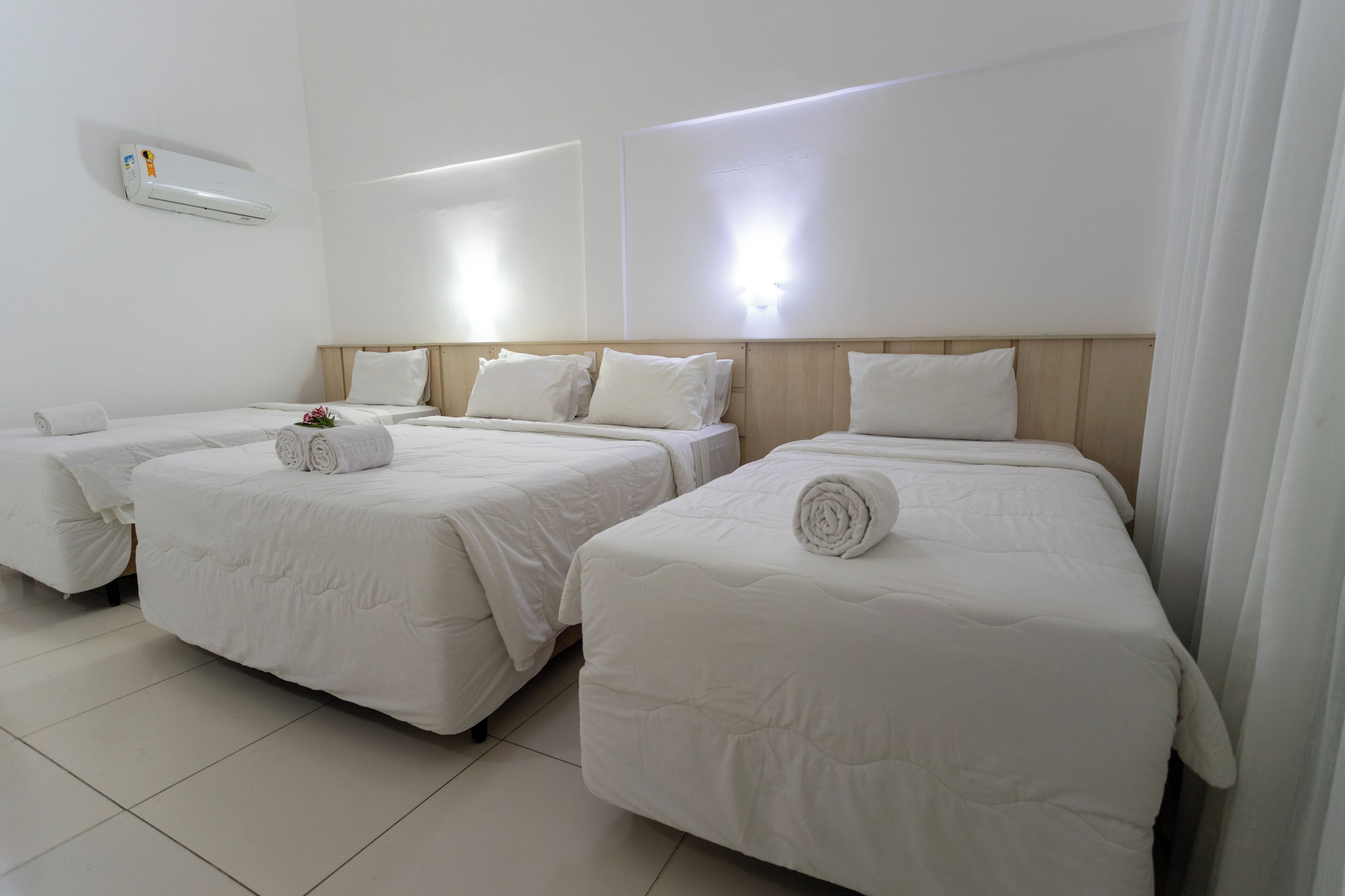 A hotel room with three beds, each with white bedding and rolled towels.