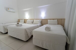 Habitación de hotel con tres camas, cada una con ropa blanca y toallas enrolladas.