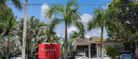 A hotel with a red sign, palm trees, and parked cars.