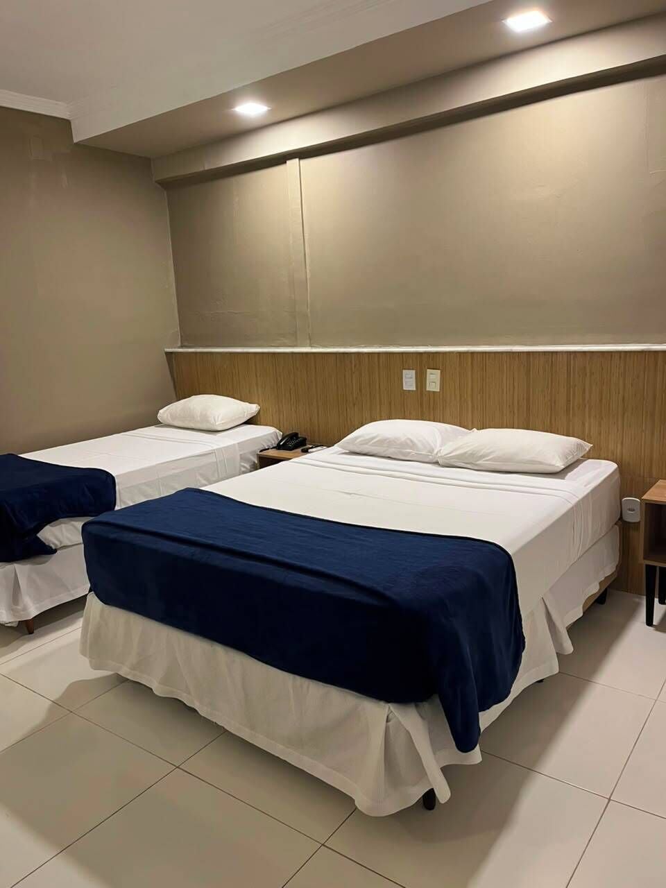 Habitación de hotel con dos camas, cada una con colchón blanco y ropa de cama azul.