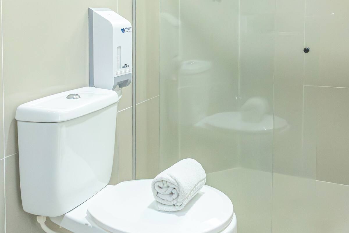 A modern bathroom with a white toilet, a glass shower enclosure, and a hand dryer mounted on the wall.