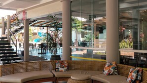 A modern lounge area with wicker furniture, large windows, and a view of outdoor seating.