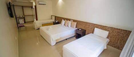 A hotel room with two beds, a small desk, a chair, a wardrobe, and an air conditioning unit.