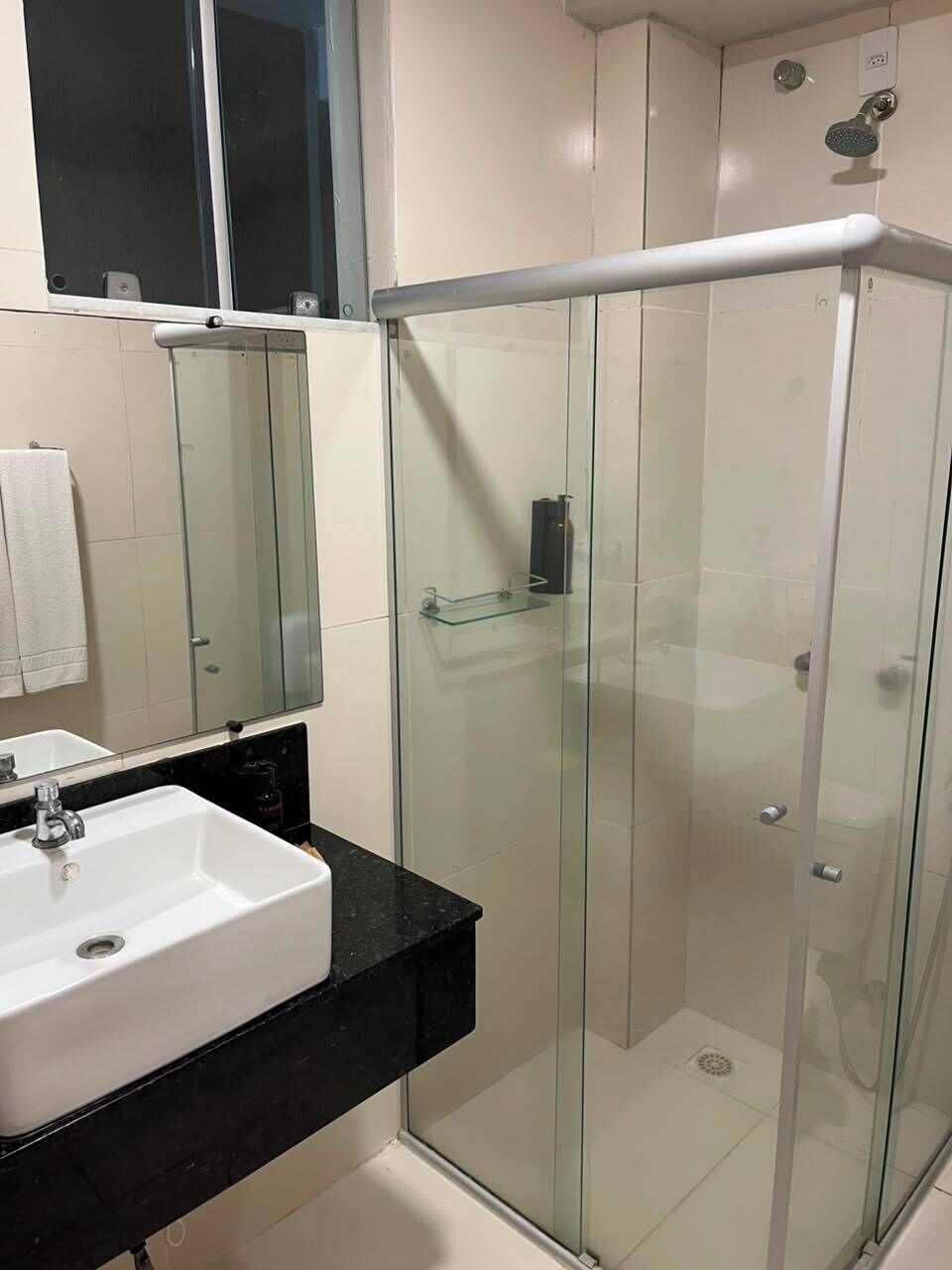Een moderne badkamer met een douchecabine van glas, een wit wastafelmeubel en een zwart aanrecht.