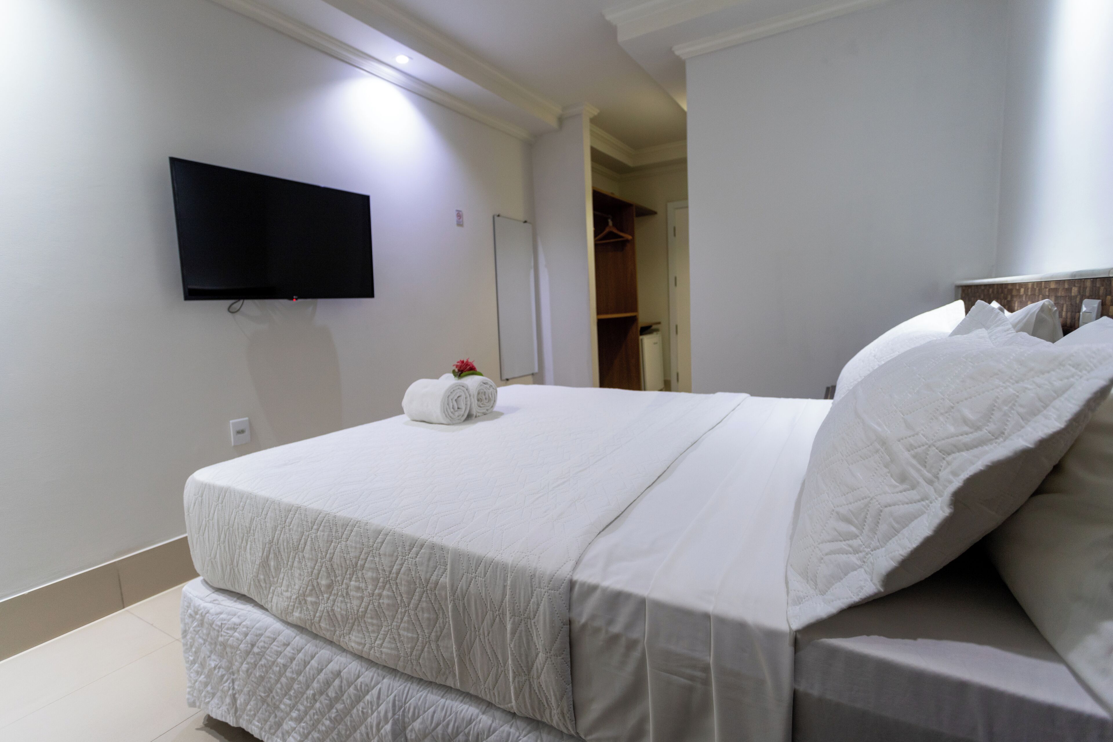 Una habitación de hotel con una cama, un televisor de pantalla plana en la pared y un vestidor.