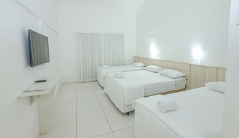 Habitación de hotel con dos camas, televisión, control remoto y ventana con cortinas.