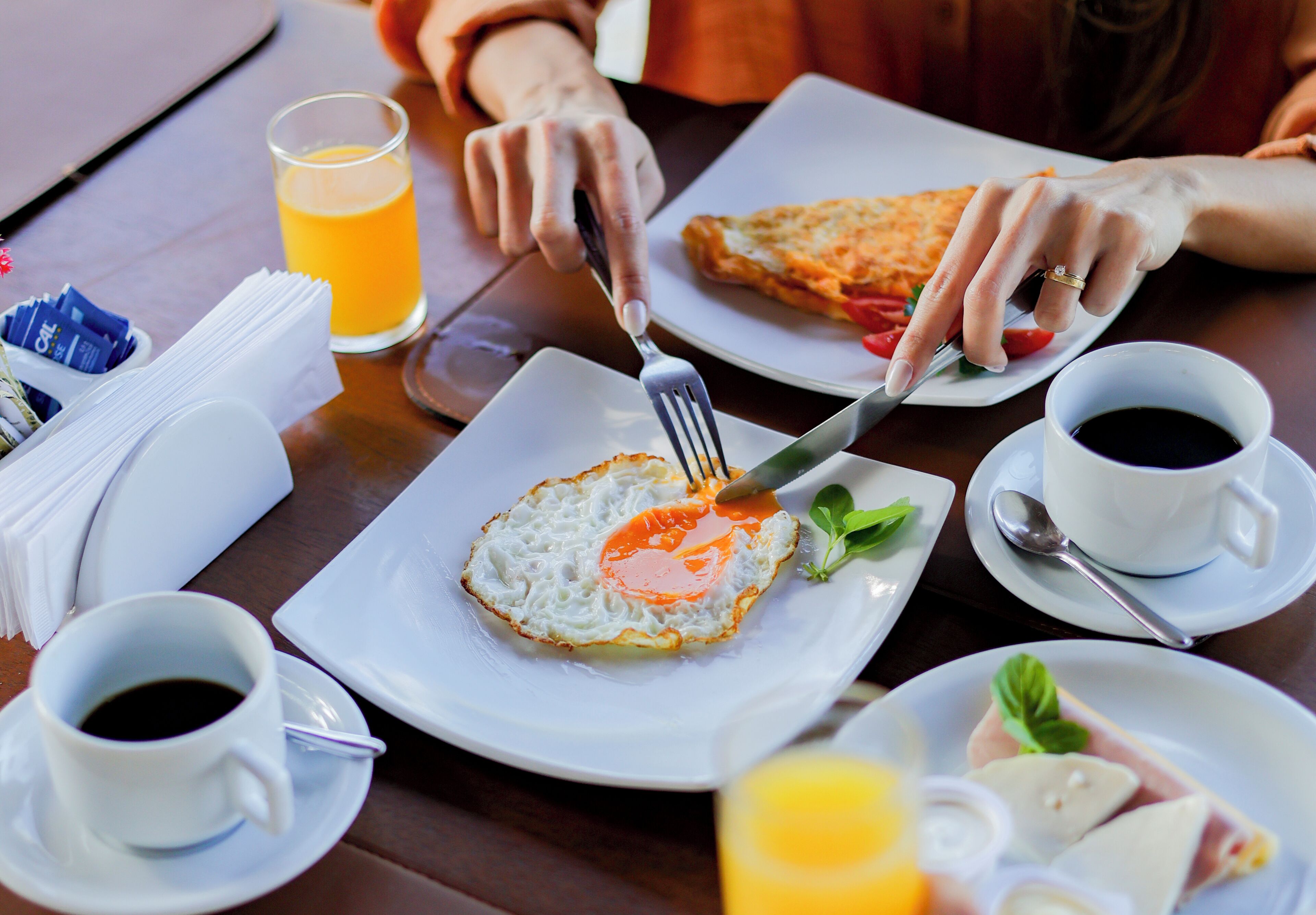 Un desayuno con un plato de huevos fritos, un vaso de jugo de naranja y una taza de café sobre una mesa de madera.
