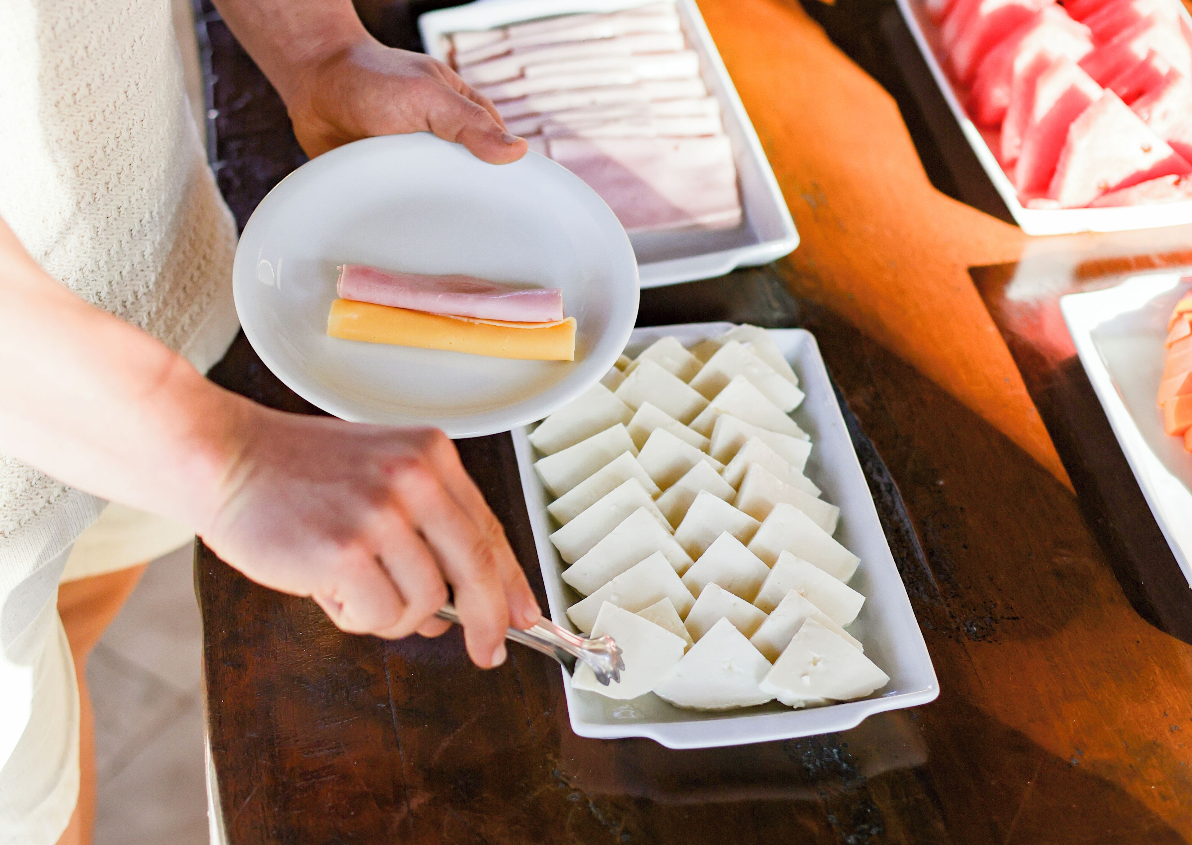 A person serving food from a white plate onto a tray.