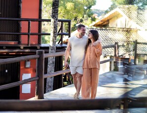 Un couple se promène sur un pont en bois muni d’une rambarde, avec un bâtiment rouge et une zone abritée en arrière-plan.