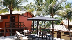 Un patio con mobiliario exterior, una zona de estar cubierta y vistas a un edificio con techo de tejas.