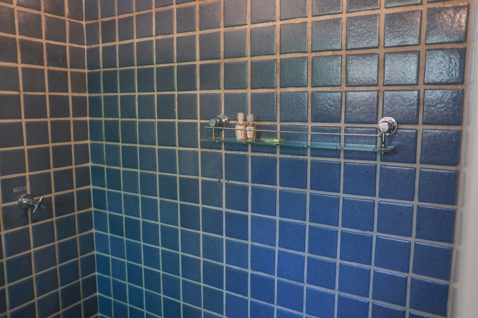 A bathroom with blue tiles and a glass shelf holding toiletries.