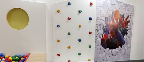A room with a climbing wall, a ball pit, and a Spider-Man artwork.