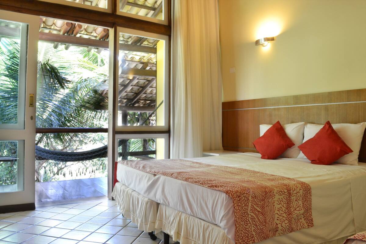 Hotelkamer met een bed, een hangmat, uitzicht op palmbomen en een deur naar buiten.
