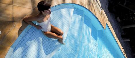 A person sitting on the edge of a swimming pool with a tiled floor and a curved edge.