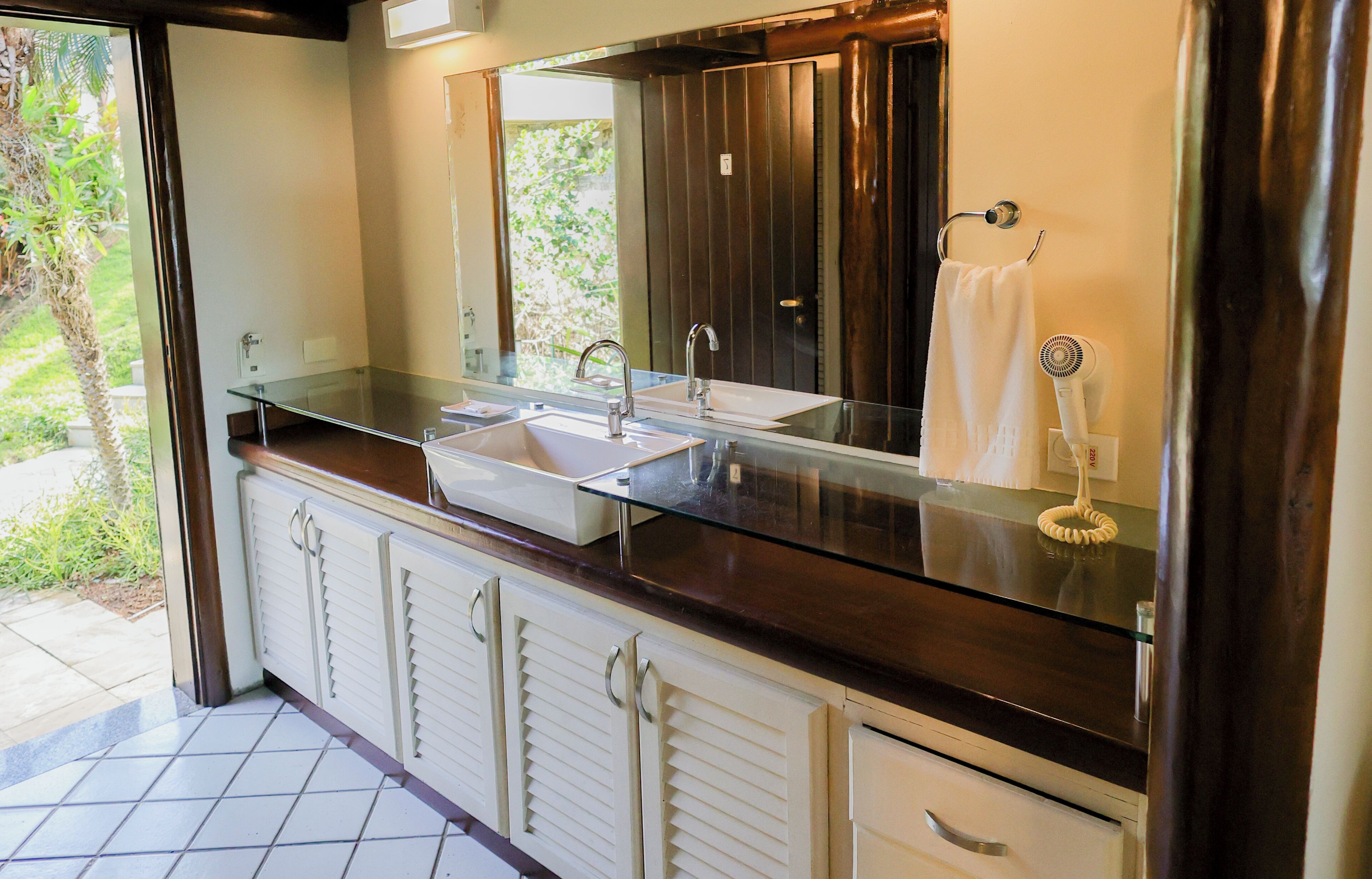 A bathroom with a glass countertop, two sinks, a large mirror, and a towel rack.