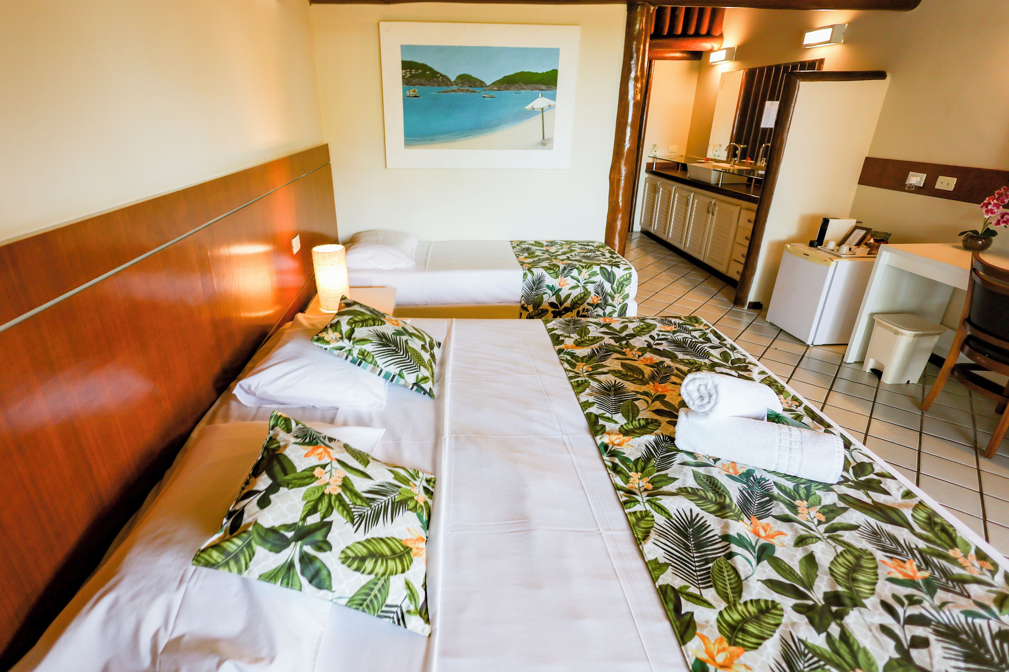 A hotel room with a bed, a desk, a chair, a small table, and a painting on the wall.