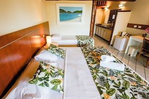 A hotel room with a bed, a desk, a chair, a small table, and a painting on the wall.